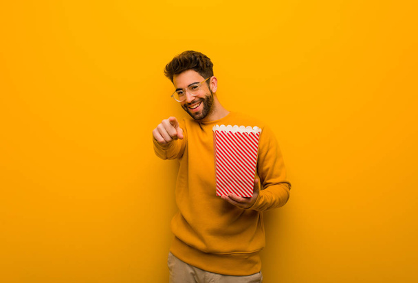 Young man holding popcorns cheerful and smiling - Foto, afbeelding