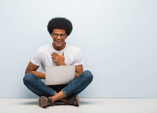 Joven hombre negro sentado en el suelo con un portátil riendo y divirtiéndose
 - Foto, Imagen