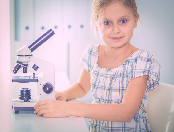 Schoolgirl looking through microscope in science class. - Zdjęcie, obraz