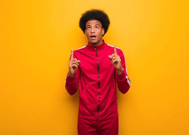 Young sport black man over an orange wall surprised pointing up to show something - Photo, Image