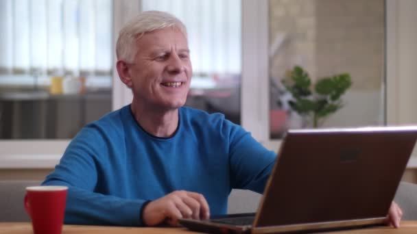 Closeup shoot of aged caucasian man typing on the laptop smiling happily indoors in a cozy apartment - Video, Çekim