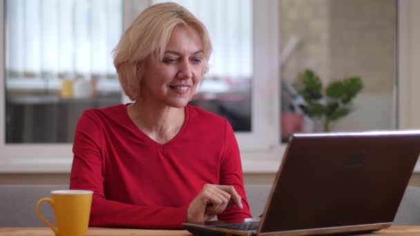 Zbliżenie strzelać w wieku kaukaski kobieta wpisując na laptopa w pomieszczeniu w przytulnym mieszkaniu - Materiał filmowy, wideo