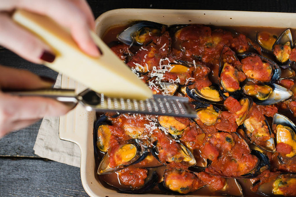 Chef rubs cheese on the mussels in tomato sauce. - Photo, Image