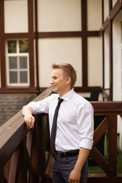 portrait of young groom man in white shirt posing on wooden balcony - Fotoğraf, Görsel
