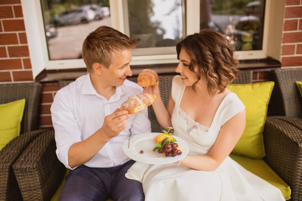 attractive young bride and groom eating delicious croissants in cafe background - Photo, image