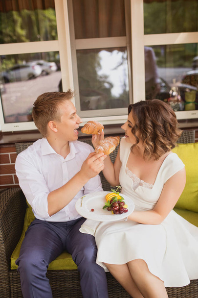 attractive young bride and groom eating delicious croissants in cafe background - Foto, immagini