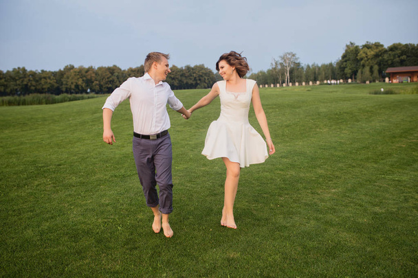 beautiful young groom and bride walking on green park with lush green grass view background - Foto, Imagen