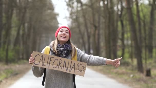Jeune femme auto-stop aller sur la route avec affiche Californie. Vue arrière
 - Séquence, vidéo