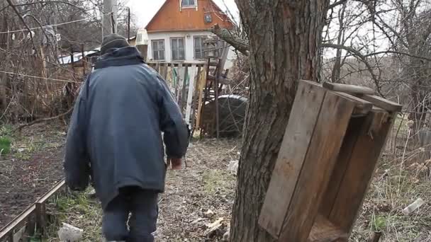 De arme oude grootvader loopt door het stukje land naar de gamrierige poort en het oude ingestorte huis. Het leven in een verlaten dorp. - Video