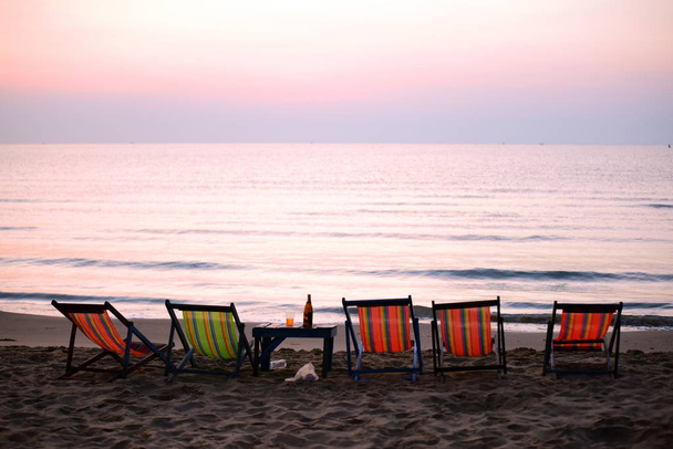 Vroege ochtend uitzicht op het strand met een lounge stoel wanneer de zon stijgt mooie gouden gele hemel en zon. Het uitzicht op het strand, het strand en de ligstoelen stijgt.  - Foto, afbeelding