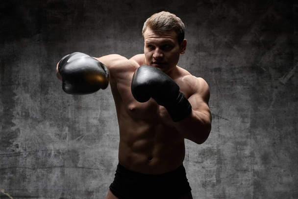 Muscular pumped man boxing in gloves on a black background. Sexy athletic body - Photo, image