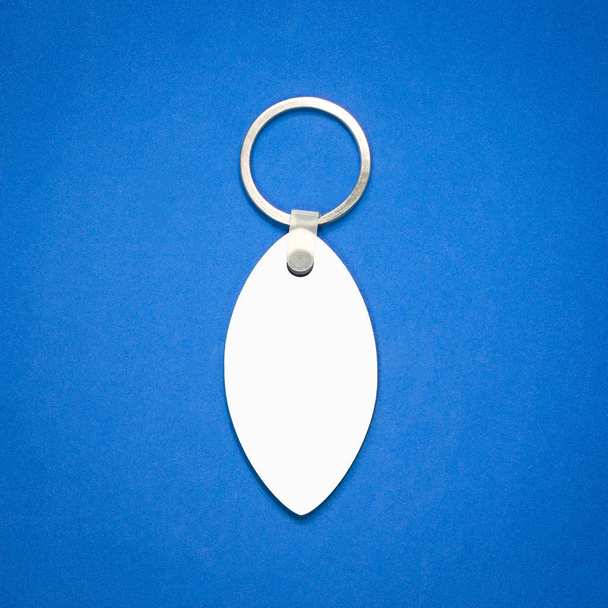 White key ring on blue background. Key chain for your design. Hanging accessory or souvenir. ( Leaf shape ) - Photo, Image