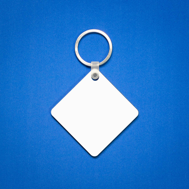 White key ring on blue background. Key chain for your design. Hanging accessory or souvenir. ( Square shape ) - Photo, Image