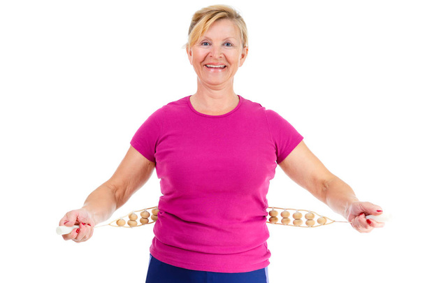 Счастливая и улыбающаяся пожилая женщина, одетая в футболку цвета Марсала делает спортивные упражнения с ручным деревянным массажером для массажа спины, изолированная на белом фоне, Положительные эмоции
 - Фото, изображение