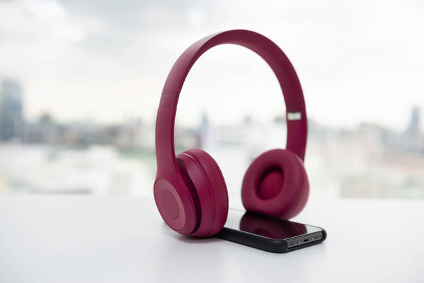 rosafarbener drahtloser Kopfhörer und Smartphone auf dem weißen Tisch - Foto, Bild