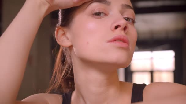 Closeup shoot of young attractive athlete female after workout being tired and looking at camera in the gym indoors - Filmati, video