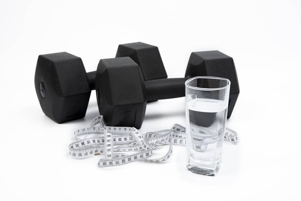 Black dumbbells, cup, and tape measure on a white background. - Photo, Image