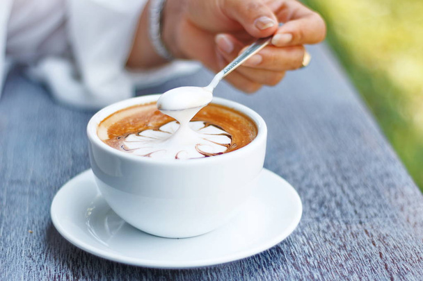 Las manos sostienen una taza de café con leche caliente sobre un fondo borroso natural
. - Foto, Imagen