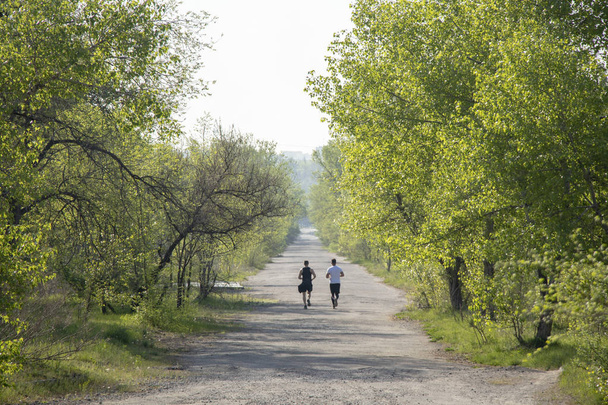 zwei junge Athleten laufen auf der Asphaltstraße in einem Park in der Stadt am Dnjepr - Foto, Bild