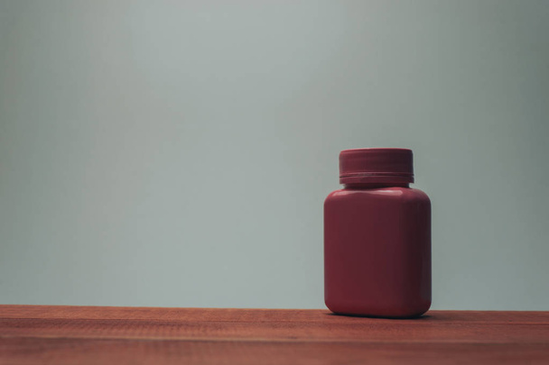 Botella rosa para pastillas sobre una mesa de madera roja y fondo gris
. - Foto, imagen