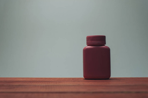Růžová láhev na tablety na červeném dřevěném stole a šedivé pozadí. - Fotografie, Obrázek