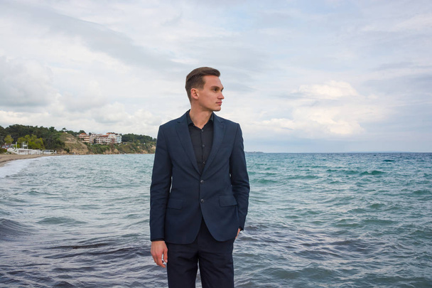 Young handsome man in a suit at the sea background and view of t - Фото, изображение