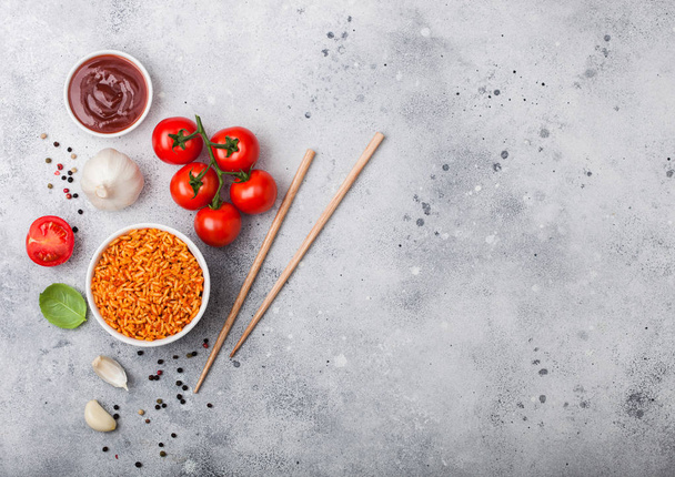 White plate bowl of rice with tomato and basil and garlic and chopsticks on light stone background. Top view. Space for text - Foto, afbeelding