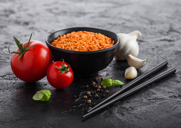 Black plate bowl of rice with tomato and basil and garlic and chopsticks on black stone background. Traditional food. - Zdjęcie, obraz