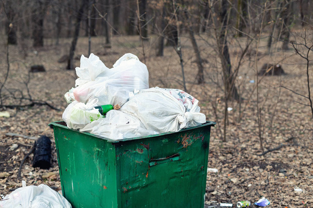 Antiguo contenedor de basura verde metálico oxidado lleno de residuos de plástico de pie en el parque de la ciudad o el bosque. Contaminación ambiental
 - Foto, Imagen