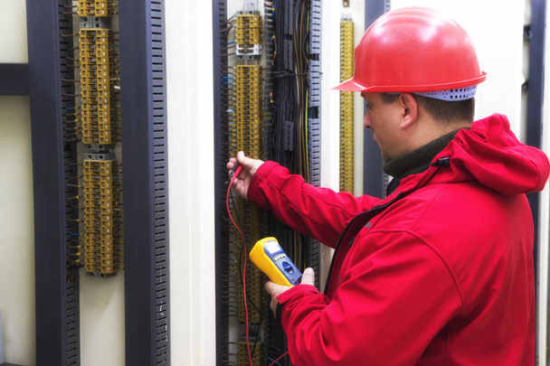 Eletricista em circuito de controle vermelho com multímetro
 - Foto, Imagem