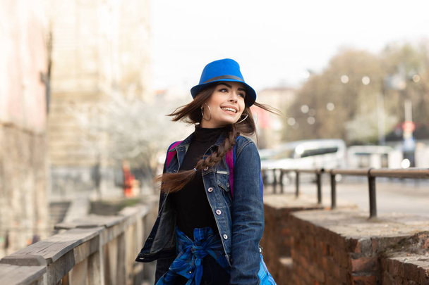Νεαρή κομψή γυναίκα που περπατά στον παλιό δρόμο της πόλης, ταξιδεύουν με σακίδιο πλάτης και μπλε καπέλο. Ουκρανία, Λβιβ - Φωτογραφία, εικόνα