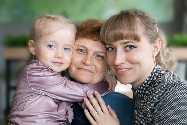 娘と孫娘は抱き合い、祖母にキスをします。小さな女の子と若い女性は、彼らの年老いたお母さんと祖母をしっかりと抱きしめる. - 写真・画像