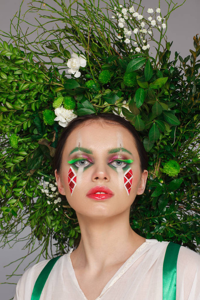 Portrait of a beautiful woman in a white dress with a green ribbon and with branches on her head. Creative makeup - Zdjęcie, obraz