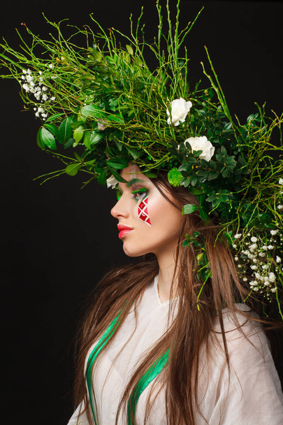Portrait of a beautiful woman in a white dress with a green ribbon and with branches on her head. Creative makeup - Foto, Imagem