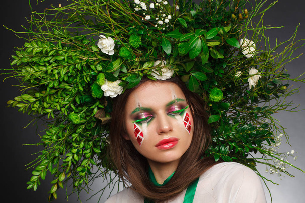 Portrait of a beautiful woman in a white dress with a green ribbon and with branches on her head. Creative makeup - Foto, immagini
