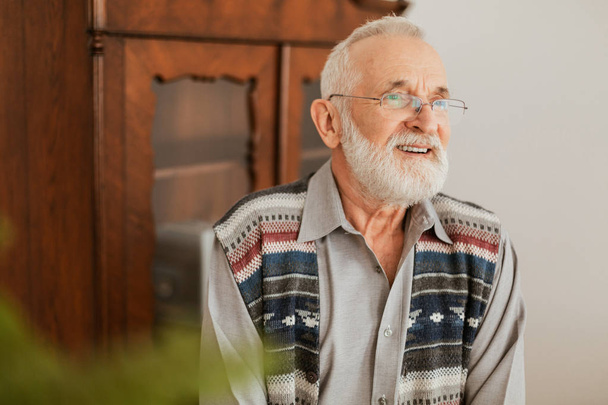 Positive senior grandfather with grey hair and beard sitting at home - Фото, зображення
