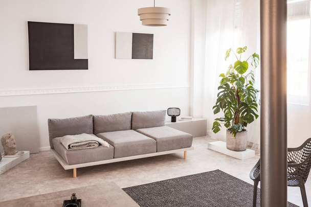 Lampada industriale nera alla moda accanto al divano scandinavo in luminoso soggiorno
 - Foto, immagini
