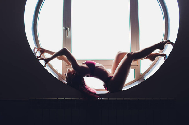 The dark silhouette of a beautiful woman on the background of the round window. yoga, acrobatics. - Фото, изображение