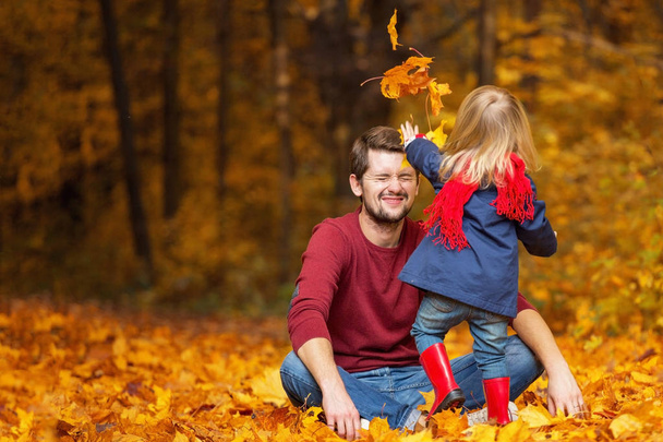 Father and daughter throw leaves in the autumn park. - 写真・画像