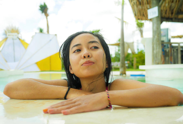 outdoors portrait of young beautiful and sweet Asian Indonesian teenager girl swimming at tropical resort pool smiling happy and cheerful enjoying relaxed holidays trip - 写真・画像