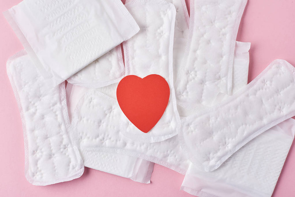 Sanitary pads with red heart on a pink background, top view - Fotó, kép