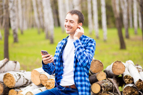 Šťastný muž na sluchátkách poslouchá hudbu a kontroluje telefony v parku - Fotografie, Obrázek