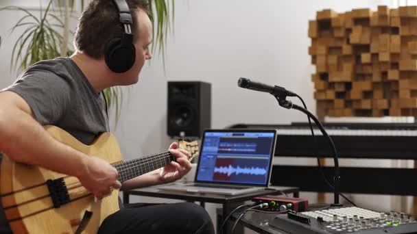 プロのミュージシャンが自宅のデジタルスタジオでエレキギターを録音。彼は歌い、楽器とミディコントローラーに囲まれています。音楽制作コンセプト.  - 映像、動画
