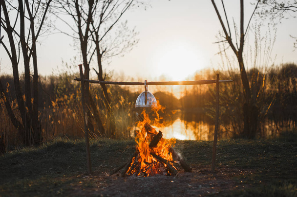 Cooking tea on a fire in a kettle at sunset - Zdjęcie, obraz