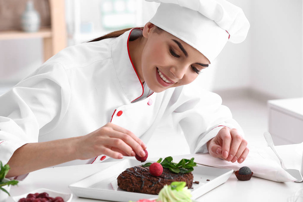 Young female confectioner decorating tasty dessert in kitchen - Photo, Image