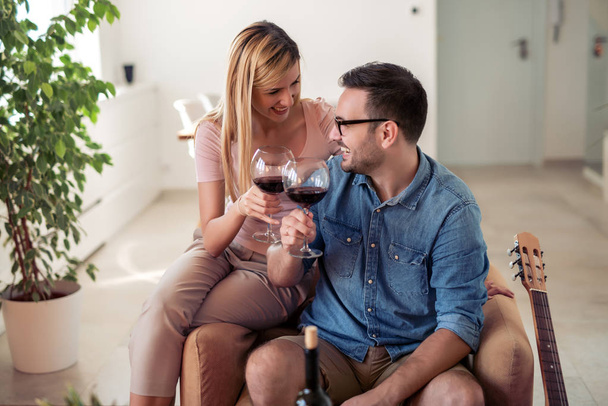 ζευγάρι πόσιμο κόκκινο κρασί στο σαλόνι στο σπίτι. - Φωτογραφία, εικόνα