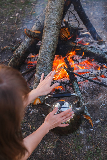 Girl warms her hands over the kettle by the fire - Photo, image