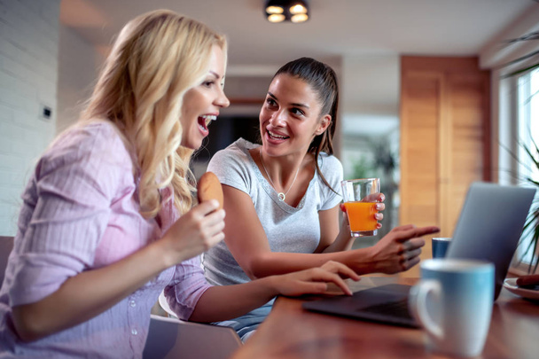 Δύο όμορφες γυναίκες απολαμβάνουν στο σπίτι και τη χρήση φορητού υπολογιστή. - Φωτογραφία, εικόνα