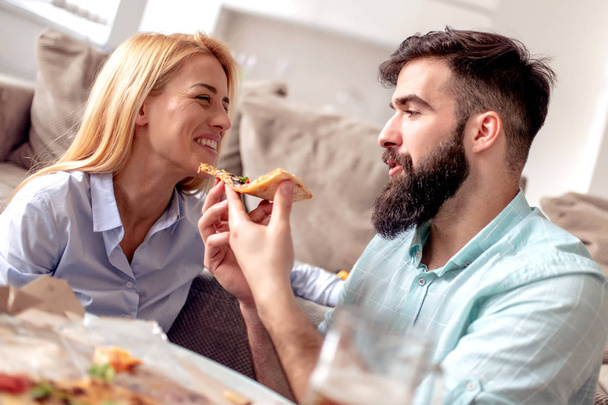 Νεαρό ζευγάρι κάθεται στο σαλόνι και τρώει πίτσα. - Φωτογραφία, εικόνα