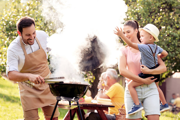 Семья устраивает барбекю в своем саду летом, наслаждаясь вместе
.  - Фото, изображение